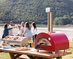Portable Alfa pizza oven placed near a lake with people having a gathering on a sunny day
